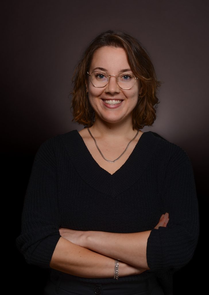 Oberkörper von Sarah mit Brille und schwarzem Pulli, lächelnd und verschränkte Arme